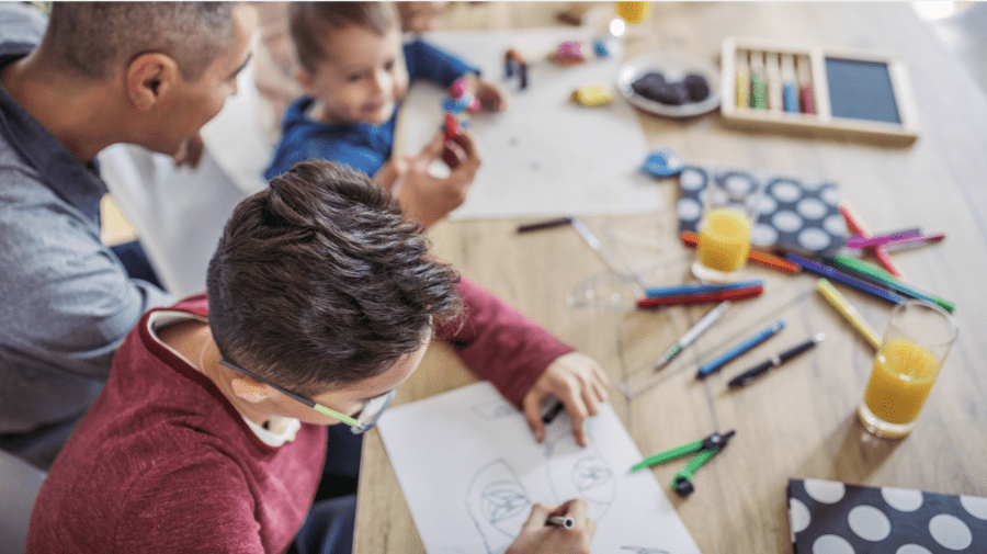 Family homeschooling together, with kids of different ages engaging in creative activities around a table filled with art supplies, paper, and learning tools.